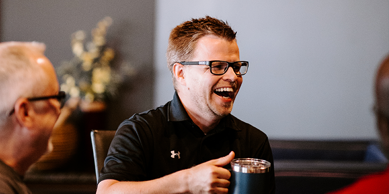 Man holding coffee laughing in a group
